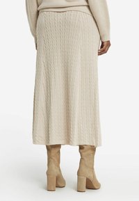 Beige kabelstickad midi kjol med strukturerat mönster, med en �åtsittande midja och flödande siluett, i kombination med knähöga stövlar med blockklack.