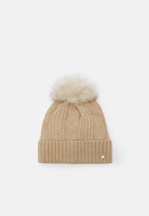 Beige knitted winter hat with cable pattern, folded ribbed brim, and large fluffy pom-pom on top.