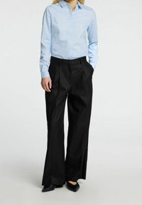 Camicia azzurra chiara con bottoni, pantaloni neri a gamba larga con pieghe, tessuto liscio e scarpe nere piatte. Design pulito senza motivi visibili.