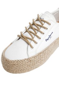 Hvit lerret espadrillesko med såle av jute-seil, med beige lisser, metall maljer og et merke i mørkeblå søm.