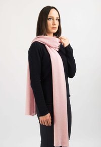 Sciarpa in cashmere di un rosa tenue, leggera e con una consistenza morbida, drappeggiata elegantemente attorno al collo, abbinata a un maglione nero.