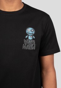 Camiseta negra de algodón con un personaje de calavera de dibujos animados azul con tibias cruzadas y un corazón, acompañado de un texto estilizado que dice "Wrong Machine".