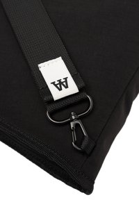 Sac en tissu noir avec une texture lisse, doté d'une sangle durable, d'un clip en métal et d'une étiquette blanche avec le logo "AA" cousu dessus.