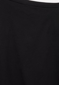 Gros plan d’un tissu noir uni avec des coutures visibles près du bord supérieur, montrant une texture lisse et des plis subtils.