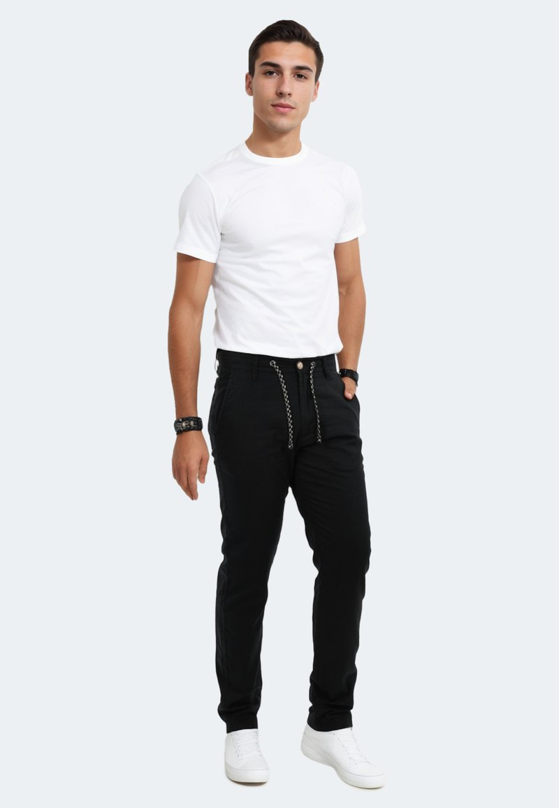 Black pants with a textured pattern and decorative chain detail, paired with a plain white t-shirt and white sneakers.