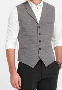 Grå houndstooth bomullsväst med kavajkrage, fem svarta knappar och spetsslut, bärs över en vit skjorta och svarta byxor.