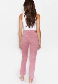 Pantalones de pana rosa con corte de pierna recta, con bolsillos traseros y una etiqueta en la cintura. Textura suave y diseño minimalista.