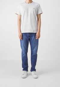 Light gray cotton t-shirt with a small black logo on the chest, paired with blue denim jeans and white sneakers.