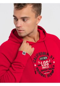 Rode katoenen hoodie met een zwarte grafische print van "CALIFORNIA ST" en "LOS ANGELES." Inclusief trekkoorden en een logo label op de mouw.