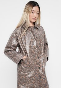 Leopard print, glossy raincoat with a collar, long sleeves, and side pockets. Features black buttons and a light brown base.