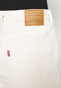 Bílé džínové kalhoty mají klasický design s koženou etiketou s nápisem "Levi Strauss & Co." a červenou nášivkou Levi's na kapse.