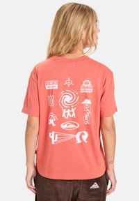 Koraal kortekorft t-shirt met witte grafische afdrukken, waaronder symbolen en tekst, ontworpen met een relaxte pasvorm en ronde hals.