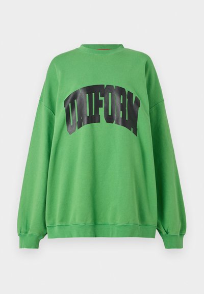 Zelená mikina vyrobená z bavlny, s zaobleným černým potiskem "UNIFORM" přes hrudník, dlouhými rukávy a uvolněným střihem.