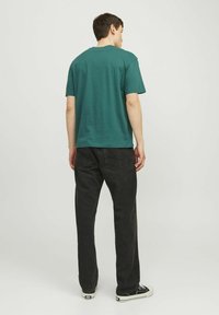 Männer T-Shirt im entspannten Schnitt aus tealfarbener Baumwolle, kombiniert mit schwarzen Jeans. Das Outfit wird mit schwarz-weißen Sneakers abgerundet.