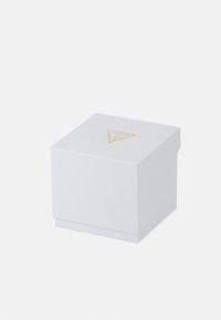 Weißer quadratischer Kasten mit einer strukturierten Oberfläche, auf dessen Oberseite sich ein dreieckiges goldenes Logo befindet. Einfaches Design ohne zusätzliche Verzierungen.