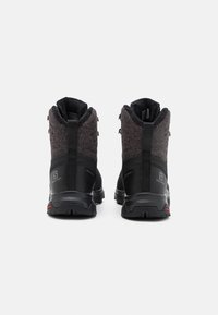 Ett par svarta och mörkgrå utemotorer med tjocka sulor, bakre dragremmar och varumärkeslogotyper visade bakifrån på en vit bakgrund.