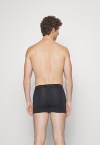 Svarte bomullsboxer med en Calvin Klein-logo i midjen, med en tettsittende design og glatt tekstur. Modellen vist fra baksiden.