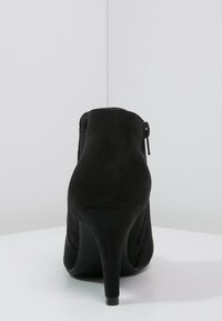 Stivaletto in suede nero con tacco alto, dotato di cerniera laterale e texture liscia. Il design è snello con punta affusolata.