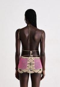 Cache-maillot en crochet beige et rose, présentant un design en filet avec des accents floraux. Se noue aux épaules et à la taille pour un ajustement personnalisé.