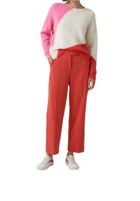 Kleurblokken trui in roze, wit en rode materialen, gecombineerd met hoge taille, felrode broeken en witte sneakers met rode accenten.