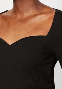 Schwarzes, geripptes Oberteil mit quadratischem Ausschnitt, langen Ärmeln und strukturiertem Stoff, der dezente vertikale Linien und eine figurbetonte Passform zeigt.