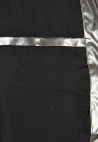 Tissu noir avec un accent argenté lisse et brillant qui court horizontalement. La texture est douce et mate, avec un détail de couture soigné.