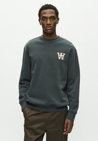 Dunkelgrauer Sweatshirt mit Rundhalsausschnitt, ausgestattet mit einem cremfarbenen Logo auf der linken Brust. Weicher Stoff sowie gerippte Bündchen und Saum.