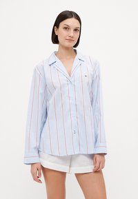 Light blue button-up shirt with red vertical stripes, featuring a collar and long sleeves. Small logo on the chest adds detail.