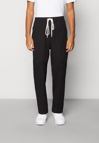 Svarta byxor med avslappnad passform, elastisk midja och vit dragsnöre. Bärs med vita sneakers. Slät textur och rak ben-design.