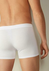 Bílé bavlněné boxerské trenýrky s hladkým povrchem a elastickým pasem, které mají těsný střih, dobře definovaný tvar a minimální švy.
