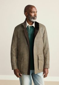 Pruuni ruuduline jakk kontrastse tumeda kraega, kahe esitaskuga ja pruuni voodriga, kihi all roheline polo särk.