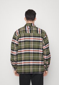 Camisa xadrez verde com riscas vermelhas, pretas e brancas; mangas longas; detalhes em botão; textura de lã; vista traseira.