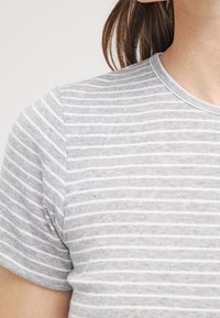 Camiseta gris de manga corta con rayas blancas horizontales. Hecha de suave algodón, con cuello redondo y textura lisa.