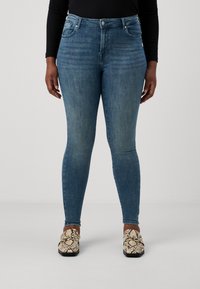 Skinny blue denim jeans with a high waist, subtle fading, and classic five-pocket design, paired with patterned slip-on shoes.