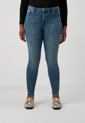Skinny blue denim jeans with a high waist, subtle fading, and classic five-pocket design, paired with patterned slip-on shoes.