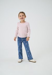 Striped pink and white long-sleeve shirt paired with blue jeans featuring pink heart patterns, completed with white shoes.