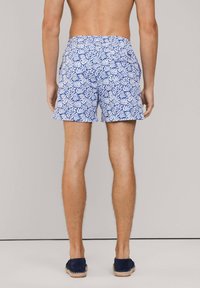 Patronen zwembroek met blauwe en witte bladdesigns, elastische tailleband en zijzakken. G gedragen met marineblauwe espadrilles.