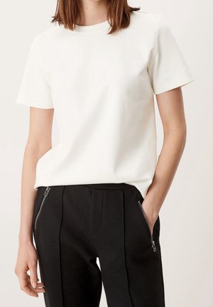 Hvid T-shirt med korte ærmer lavet af blødt materiale, med klassisk rund halsudskæring, parret med sorte skræddersyede bukser med lynlåslommer.