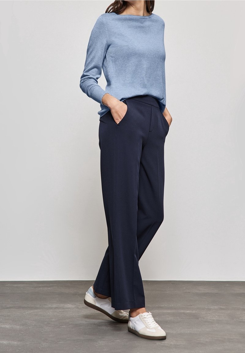 Vaaleansininen pitkähihaisuus neule, tummansiniset leveälahkeiset housut ja valkoiset sneakersit, joissa on harmaat yksityiskohdat. Sileä pinta, rento istuvuus, sivutaskut.