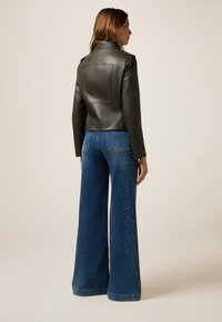 Jachetă din piele ecologică neagră, cu un design ajustat, asociată cu blugi albastri cu picioare largi, având embellishments cu ținte pe laterale.