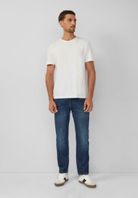 Biała bawełniana koszulka, okrągły dekolt, krótki rękaw, zestawiona z ciemnoniebieskimi dżinsami. Obuwie stanowią białe trampki z brązowymi i czarnymi akcentami.