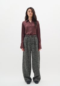 Burgundi selyem ing, gallérral és gombos záródással, széles szárú, tapintású houndstooth nadrággal és fekete övvel kombinálva. Fekete cipő.