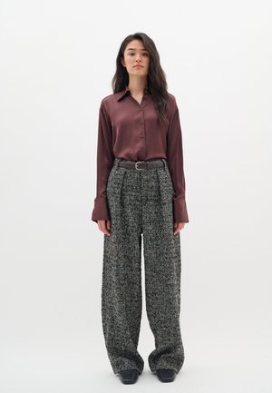 Bordeauxrot hose Satinhemd mit Kragen und Knopfverschluss, kombiniert mit weit geschnittenen, strukturierten Hahnentritthosen und einem schwarzen Gürtel. Schwarze Schuhe.