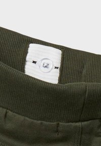 Ceinture en tissu côtelé vert olive avec une étiquette blanche présentant un bouton clair et des coutures. Vue rapprochée mettant en avant la texture et les détails.