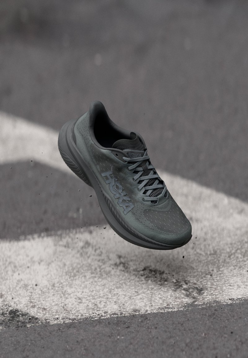 Black running shoe with textured upper, thick sole, and prominent logo. Features a padded collar and laces for secure fit.