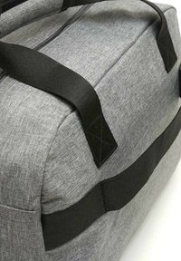 Graue Stoff-Duffel-Tasche mit schwarzen Trägern, rechteckiger Form, strukturierten Oberflächen und verstärkten Ecken. Sichtbarer Reißverschluss.