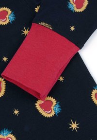 Manica di camicia di cotone con polsino rosso. Sfondo blu navy con motivi decorativi di cuori dorati e rossi, accenti verdi e stelle gialle.