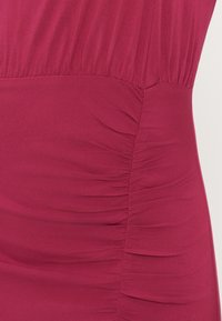 Κοντινή λήψη κόκκινου υφασμάτινου ενδύματος με ραμμένες πιέτες κατά μήκος μιας κάθετης ραφής.