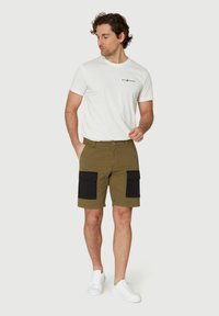 Pantalones cortos cargo verde oliva con bolsillos de parche negros, tela de algodón, cierre de cremallera y una camiseta blanca ajustada. Modelo lleva zapatillas blancas.
