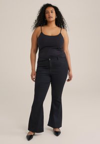 Schwarze Schlagjeans mit einer glatten Denim-Oberfläche, kombiniert mit einem taillierten schwarzen Tanktop mit dünnen Trägern.